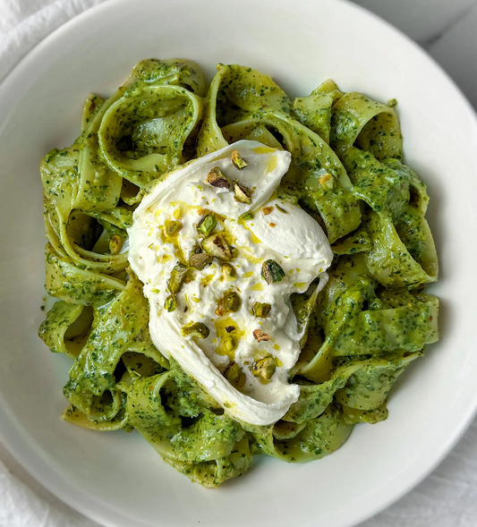 Pasta with green pesto and a dollop of white cream on a white plate.